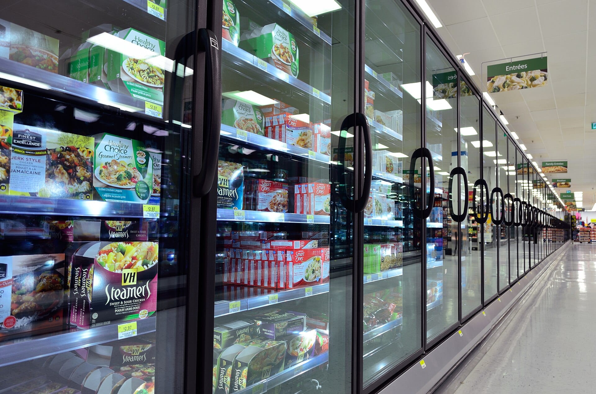 A supermarket aisle lined with glass-door refrigerators full of frozen food.