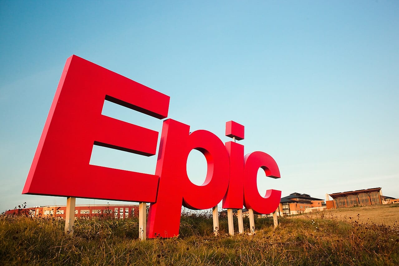 Letrero con las letras rojas de Epic Systems sobre el pasto, con edificios de la empresa al fondo.