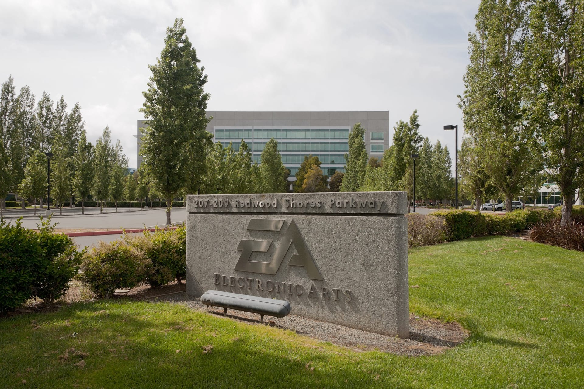 Letrero de piedra con el logotipo de Electronic Arts frente a un edificio de oficinas rodeado de árboles.
