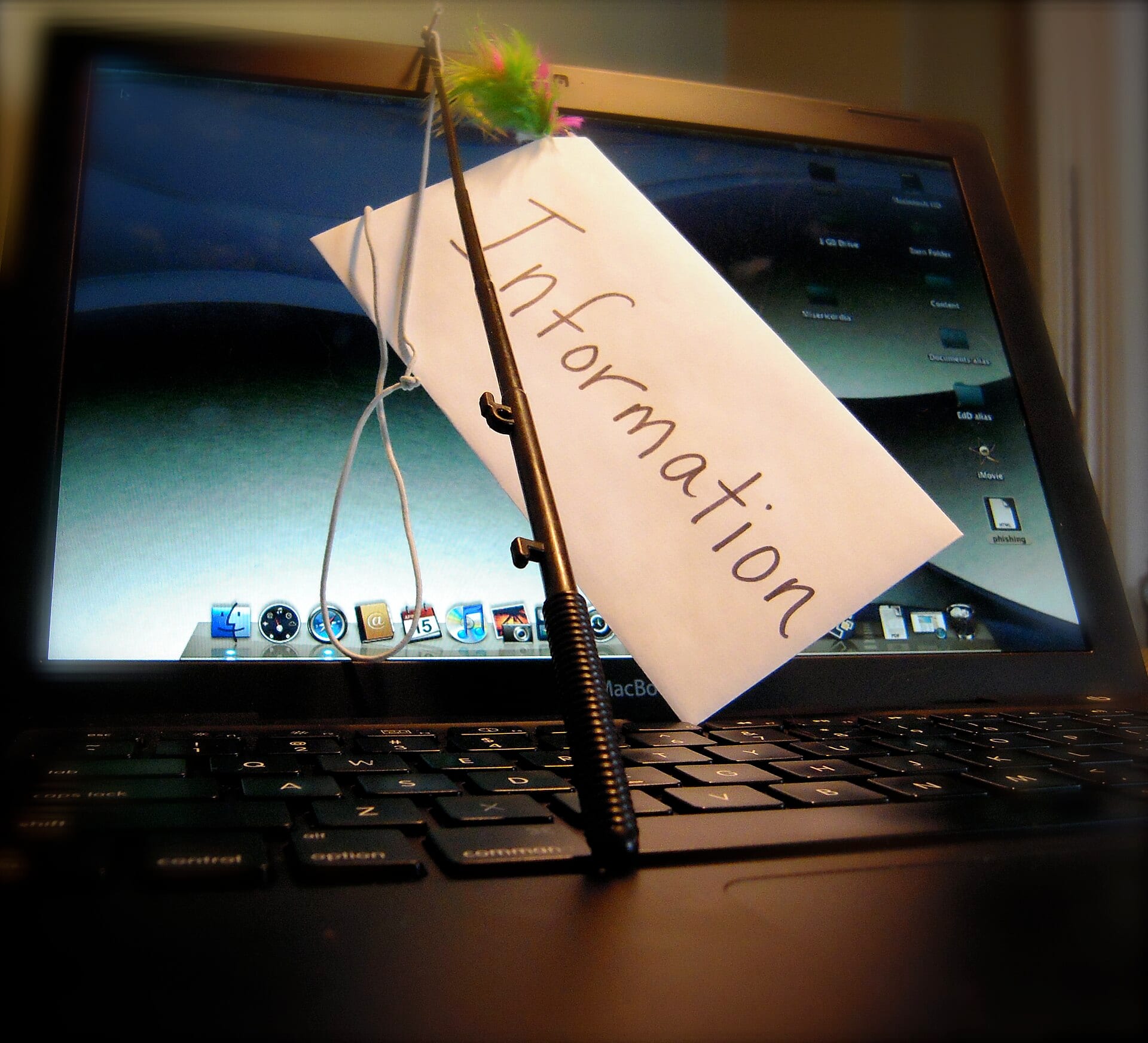 A toy fishing rod holds up an envelope marked Information in front of a laptop screen.