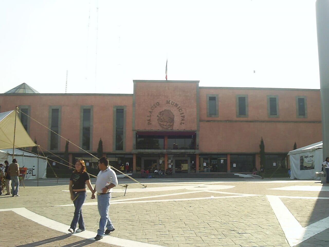 Fachada del Palacio Municipal de Ecatepec, con su explanada al frente y personas caminando por la plaza.