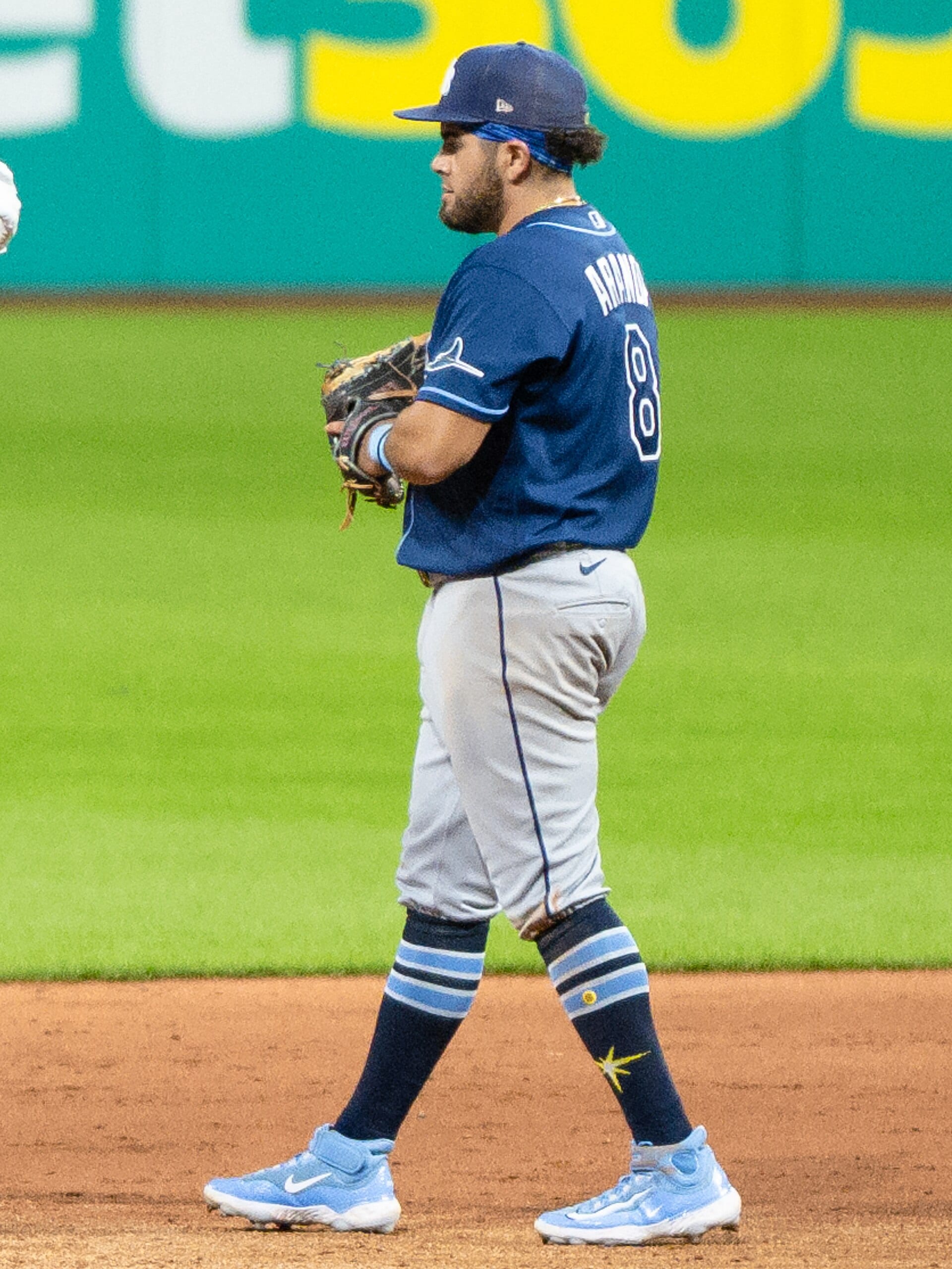 Jonathan Aranda, con el número 8 y uniforme azul marino de los Rays, de pie sobre la tierra del cuadro con el guante en la mano.