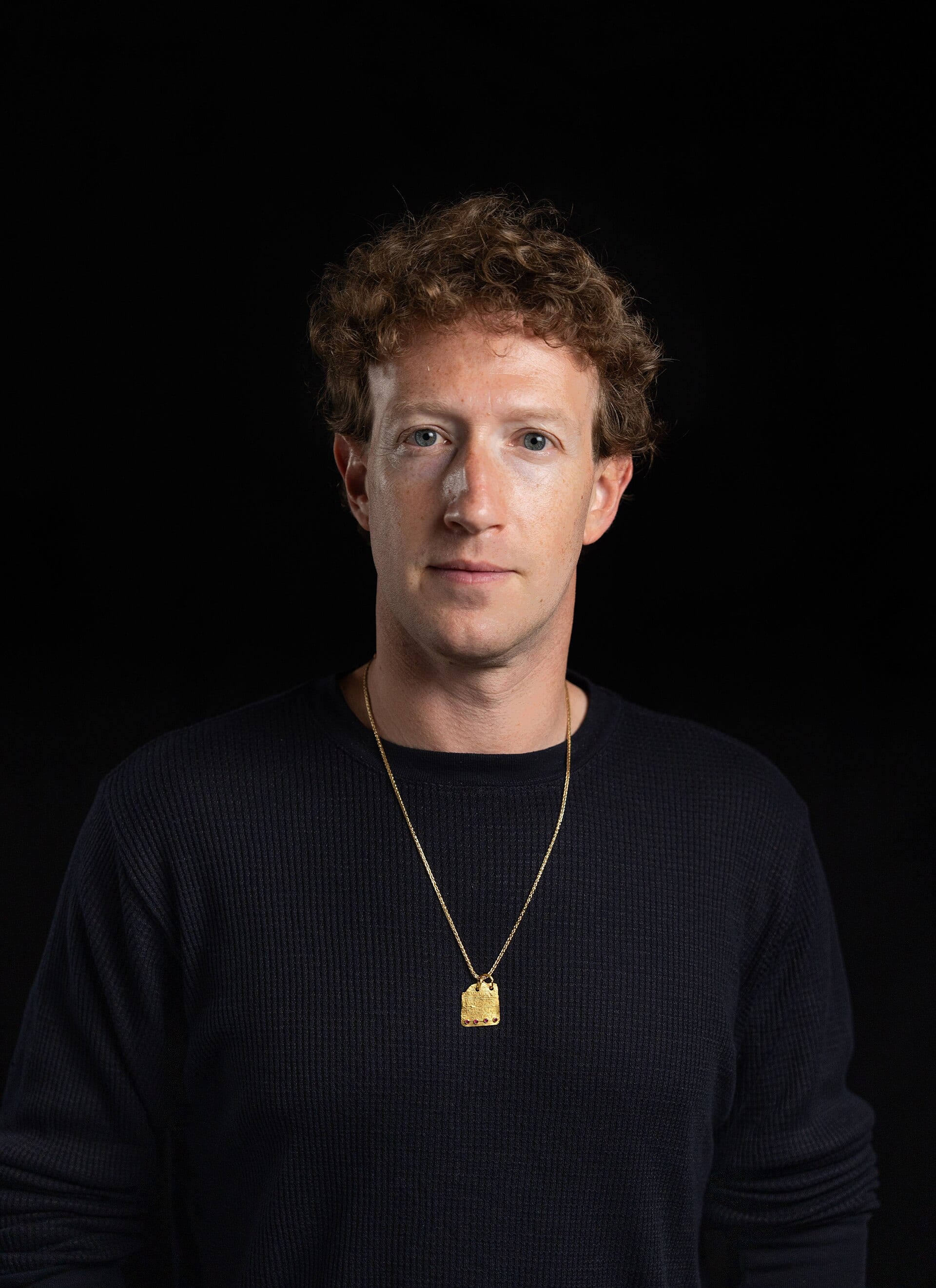 Mark Zuckerberg, con traje oscuro, mira de frente en un retrato de estudio con fondo gris liso.