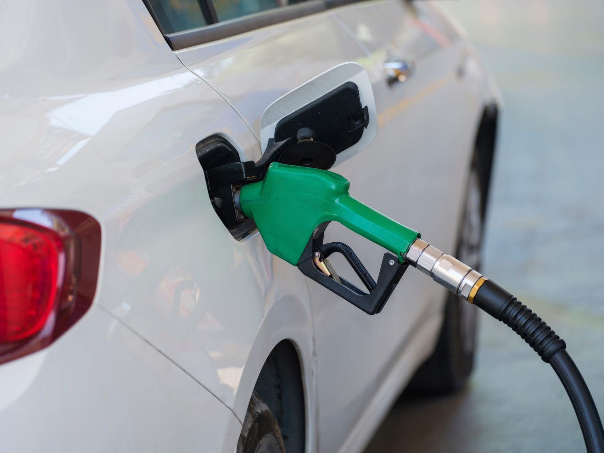 Una boquilla verde de despachador surte combustible al tanque de un auto blanco.