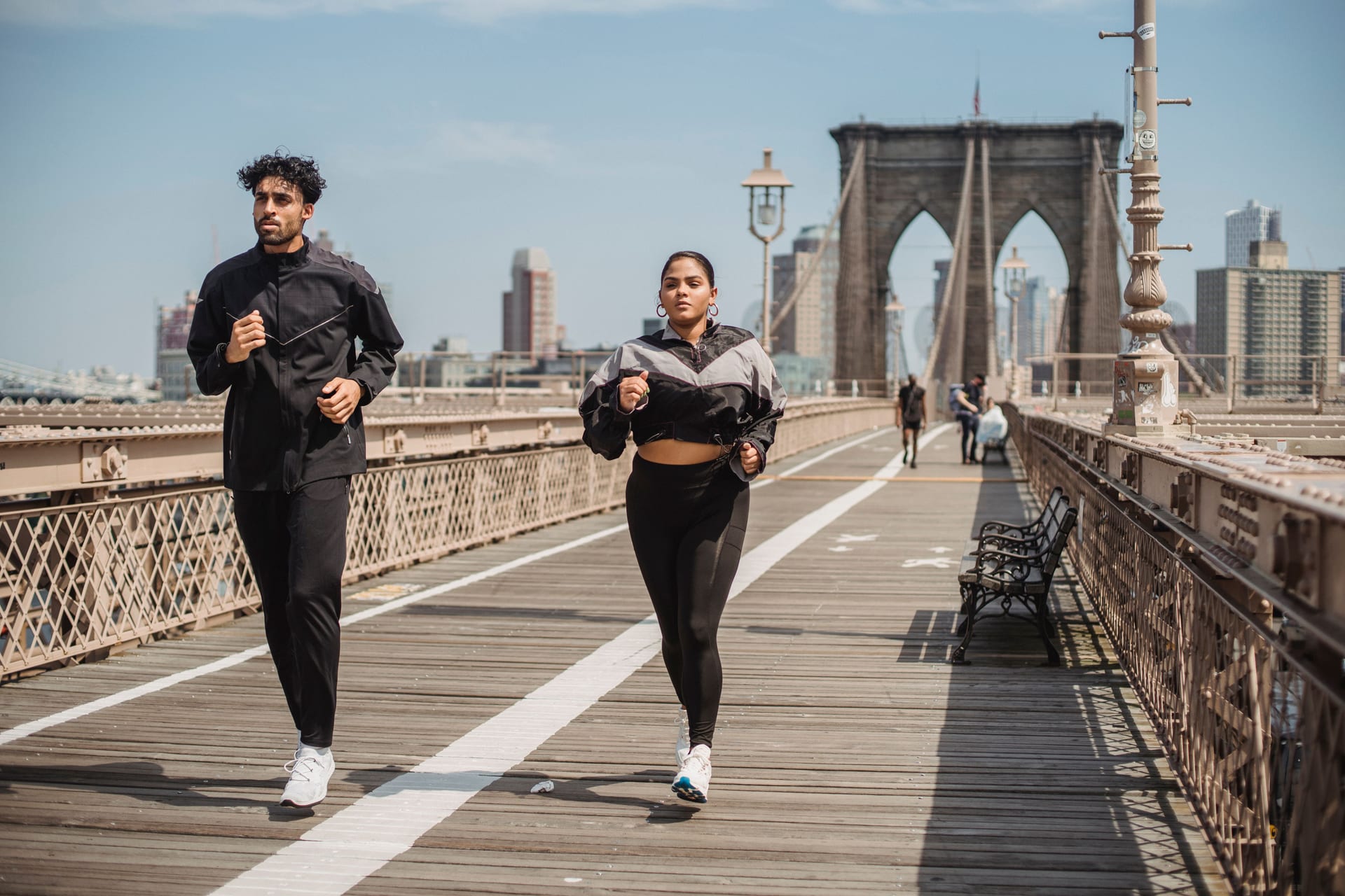 Dos personas trotan sobre el puente de Brooklyn con los rascacielos de fondo.