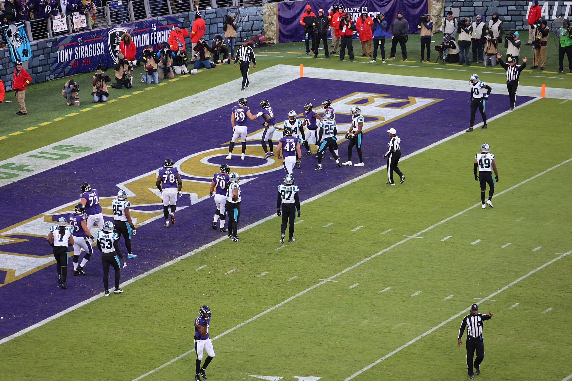 Jugadores de los Ravens celebran en la zona de anotación morada de M&T Bank Stadium mientras fotógrafos y árbitros rodean la jugada.