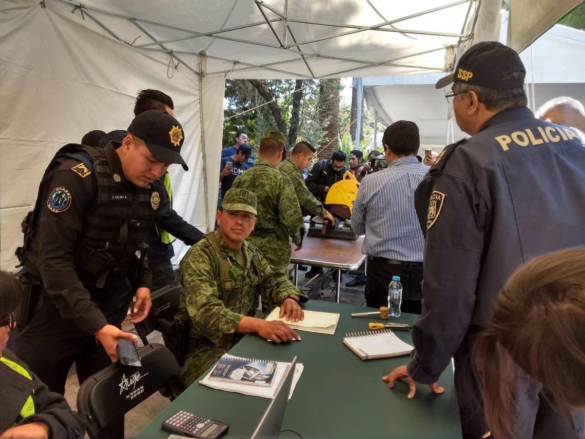 Police officers and soldiers in uniform work at a table with documents under a white tent, during a gun-control event in Mexico City.
