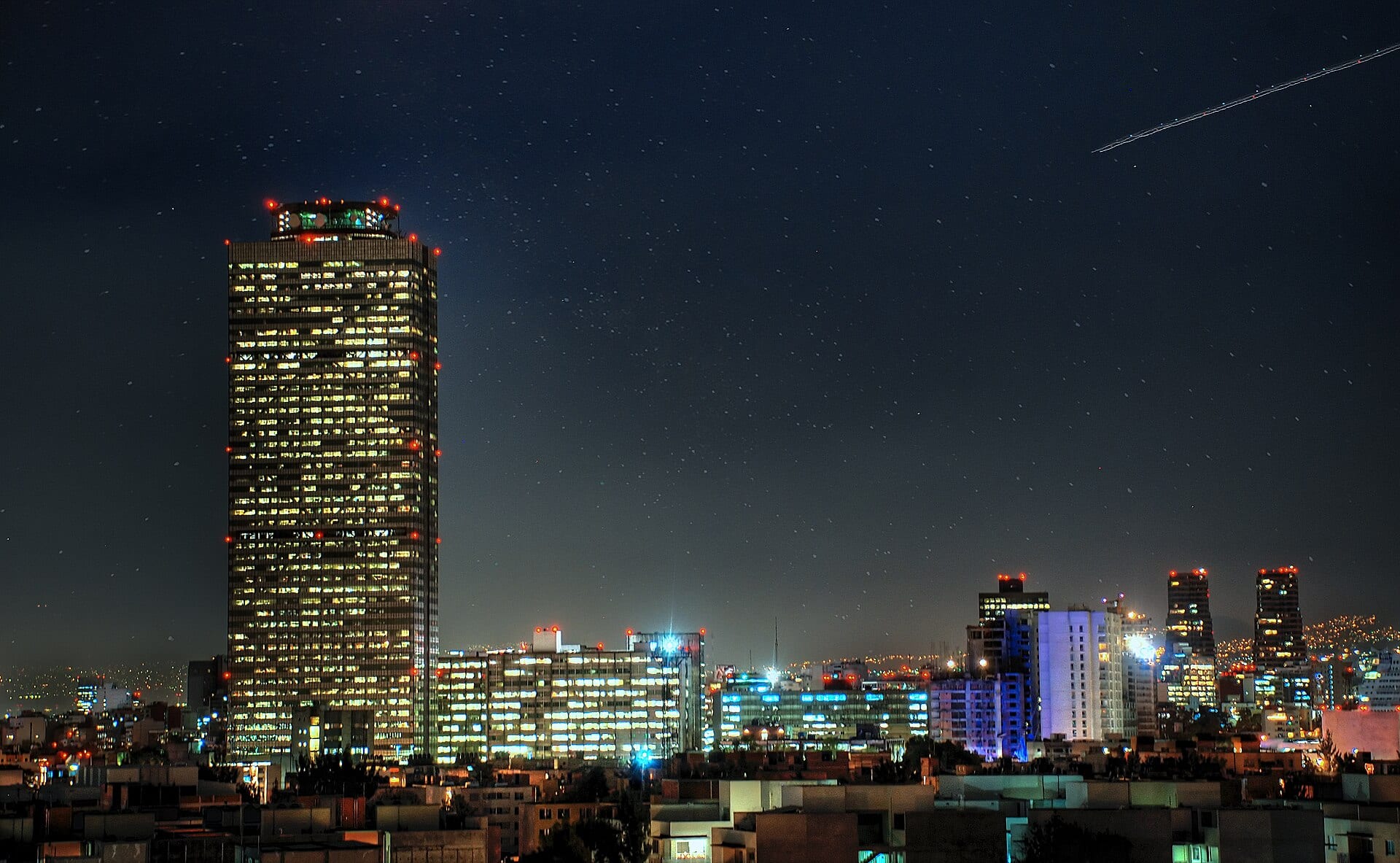 La Torre de Pemex, iluminada de noche, se eleva sobre los edificios de oficinas y las azoteas de la Ciudad de México.