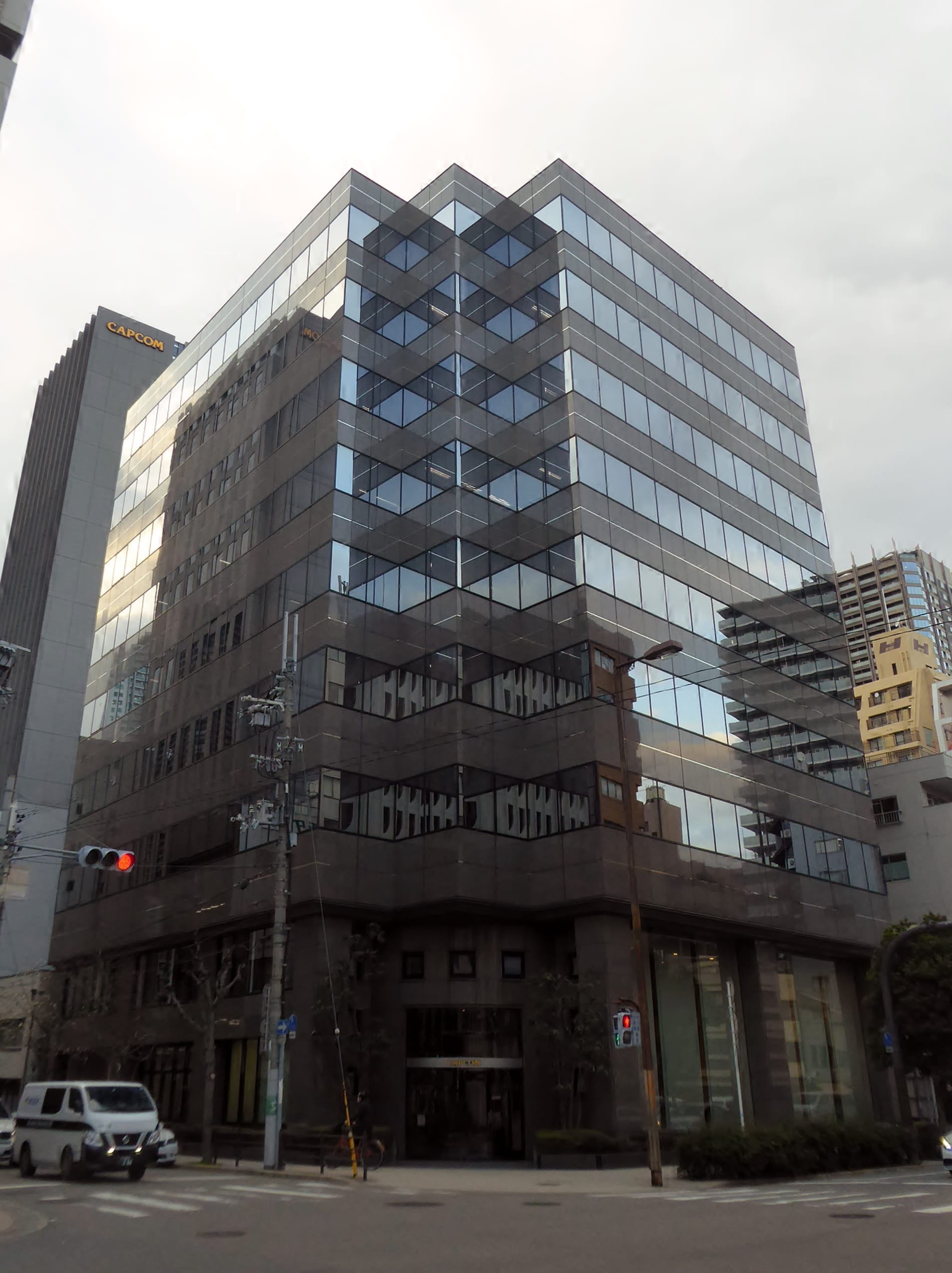 Edificio de oficinas de cristal oscuro en una esquina de Osaka, con el letrero de Capcom en la torre vecina.