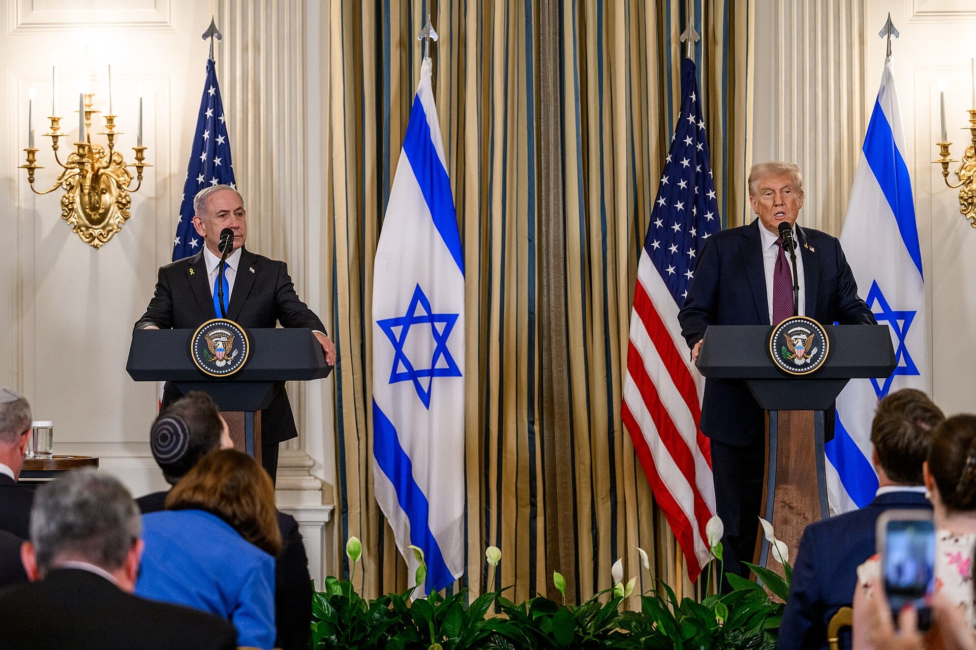 Benjamin Netanyahu, de traje oscuro, escucha de pie tras un podio con sello presidencial, entre banderas de Israel y de Estados Unidos.