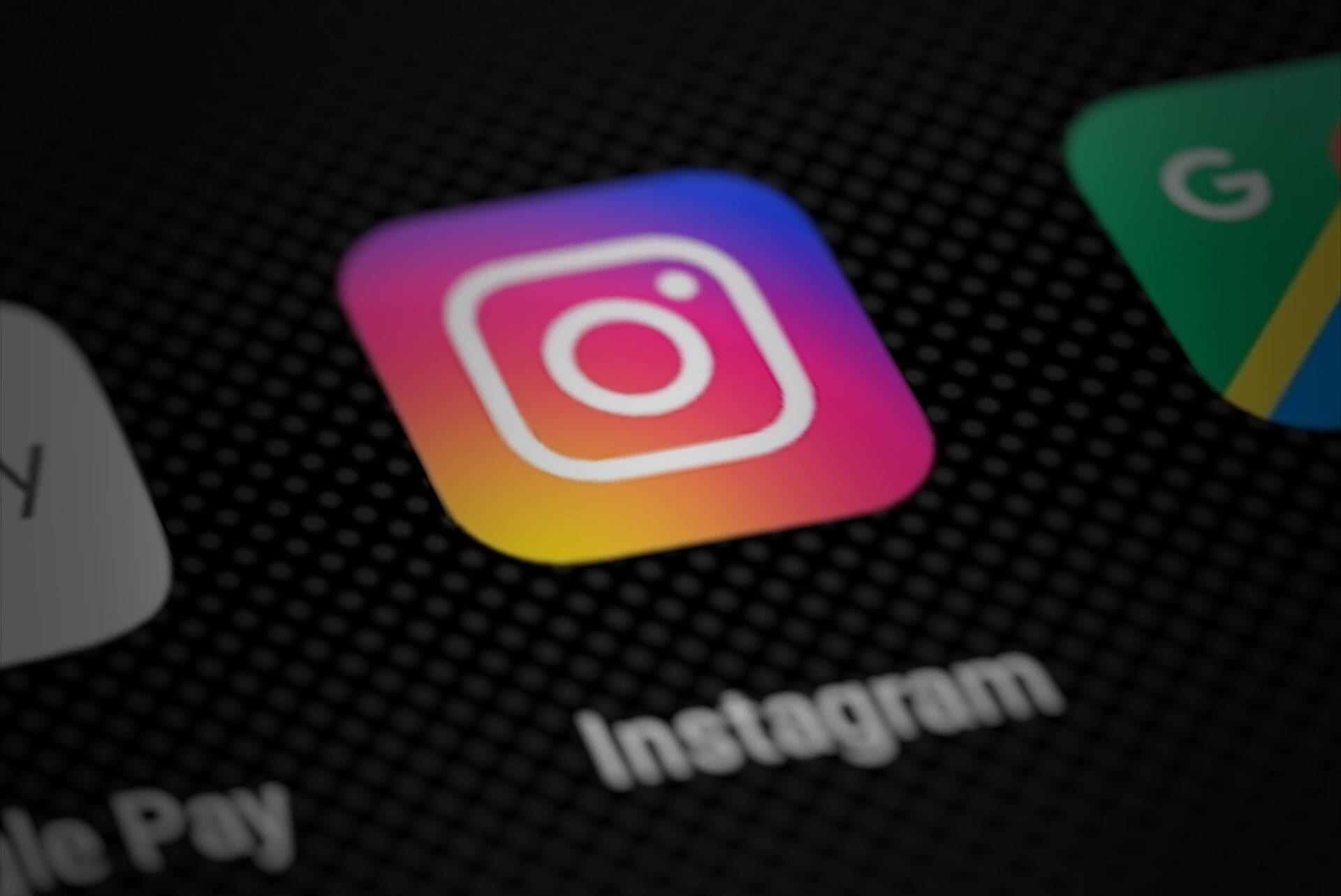 El ícono de Instagram, con su degradado de amarillo a morado, sobre la pantalla oscura de un teléfono, junto a otras aplicaciones desenfocadas.