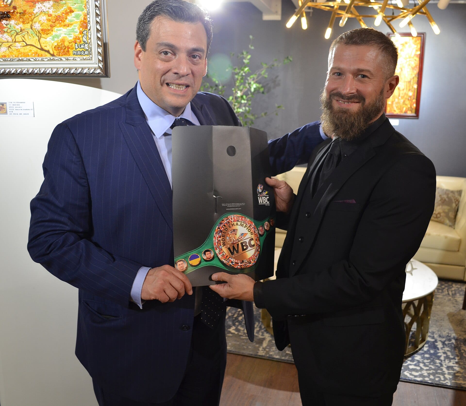 Mauricio Sulaimán, de traje azul, sostiene junto a otro hombre una caja con un cinturón verde del Consejo Mundial de Boxeo.