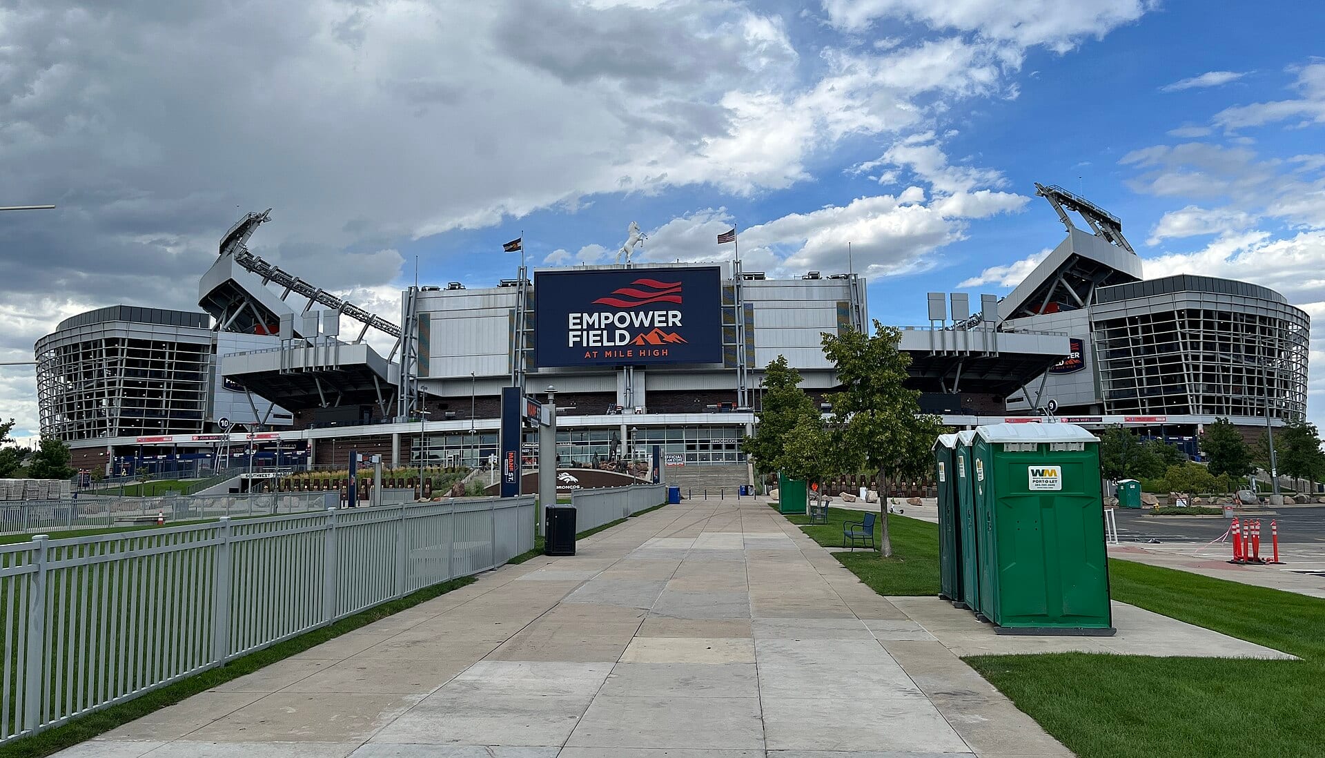 Fachada del estadio Empower Field at Mile High con su pantalla azul marino bajo un cielo nublado