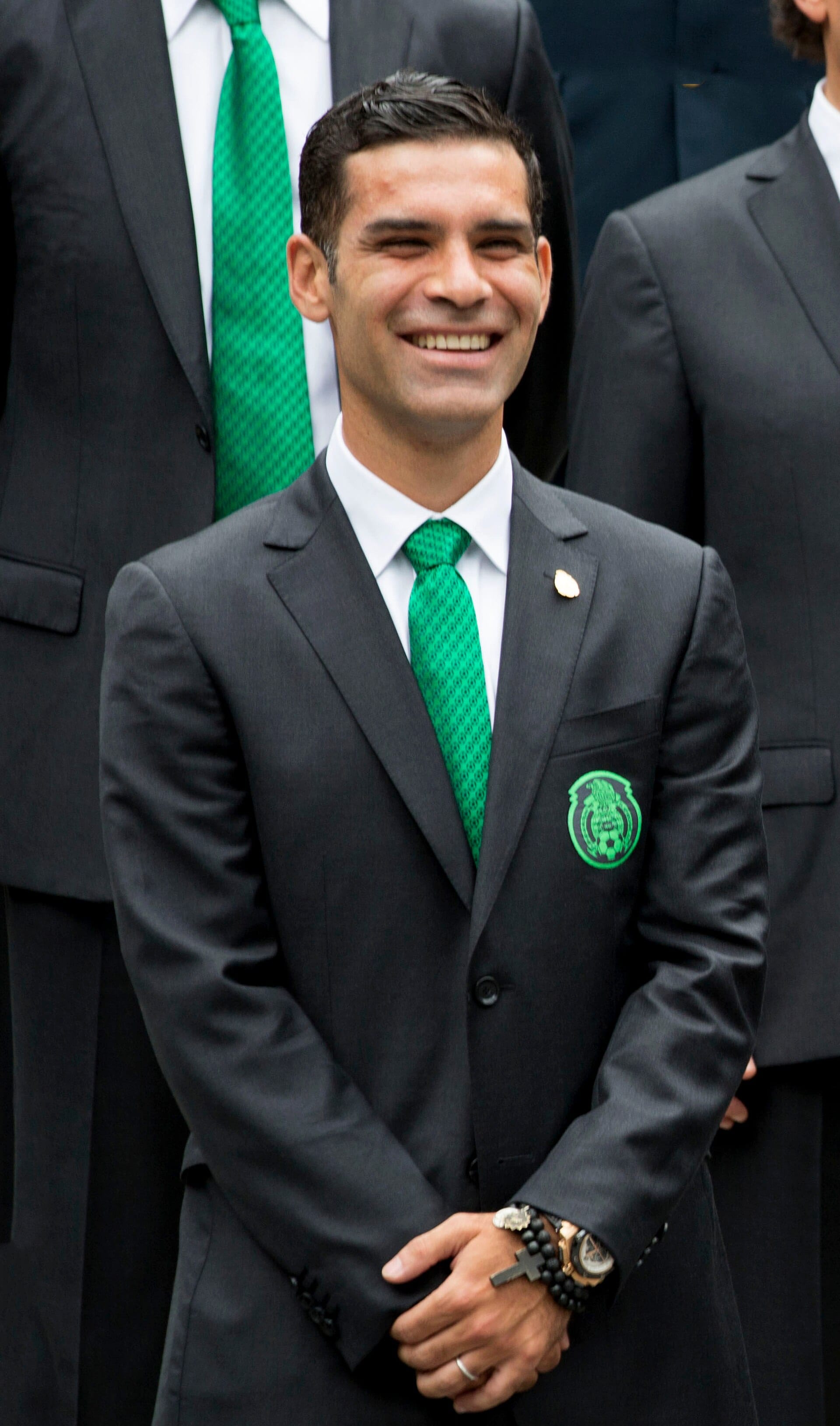 Rafael Márquez sonríe de pie con traje oscuro y corbata verde, con el escudo de la Selección Mexicana en el saco.