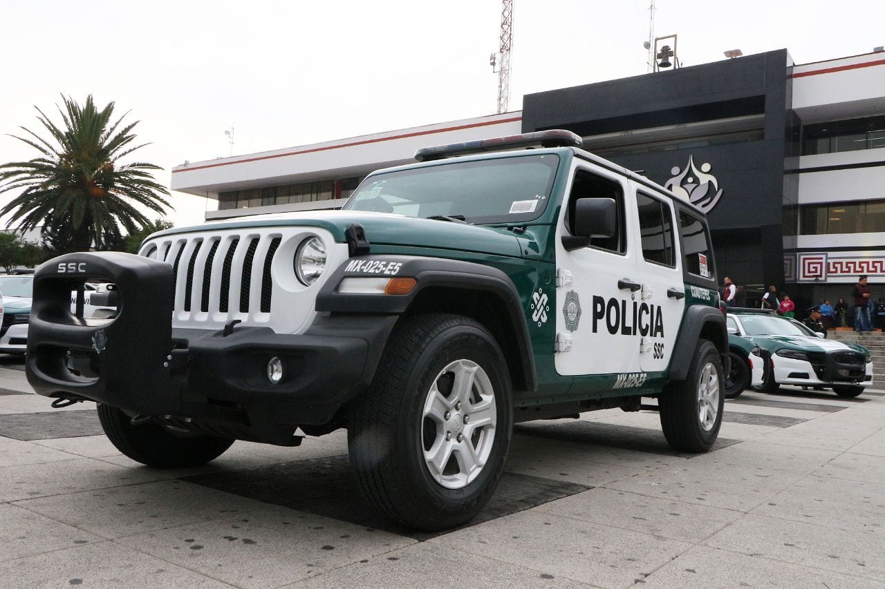 Una camioneta verde y blanca con la leyenda Policía SSC estacionada en una explanada frente a un edificio.