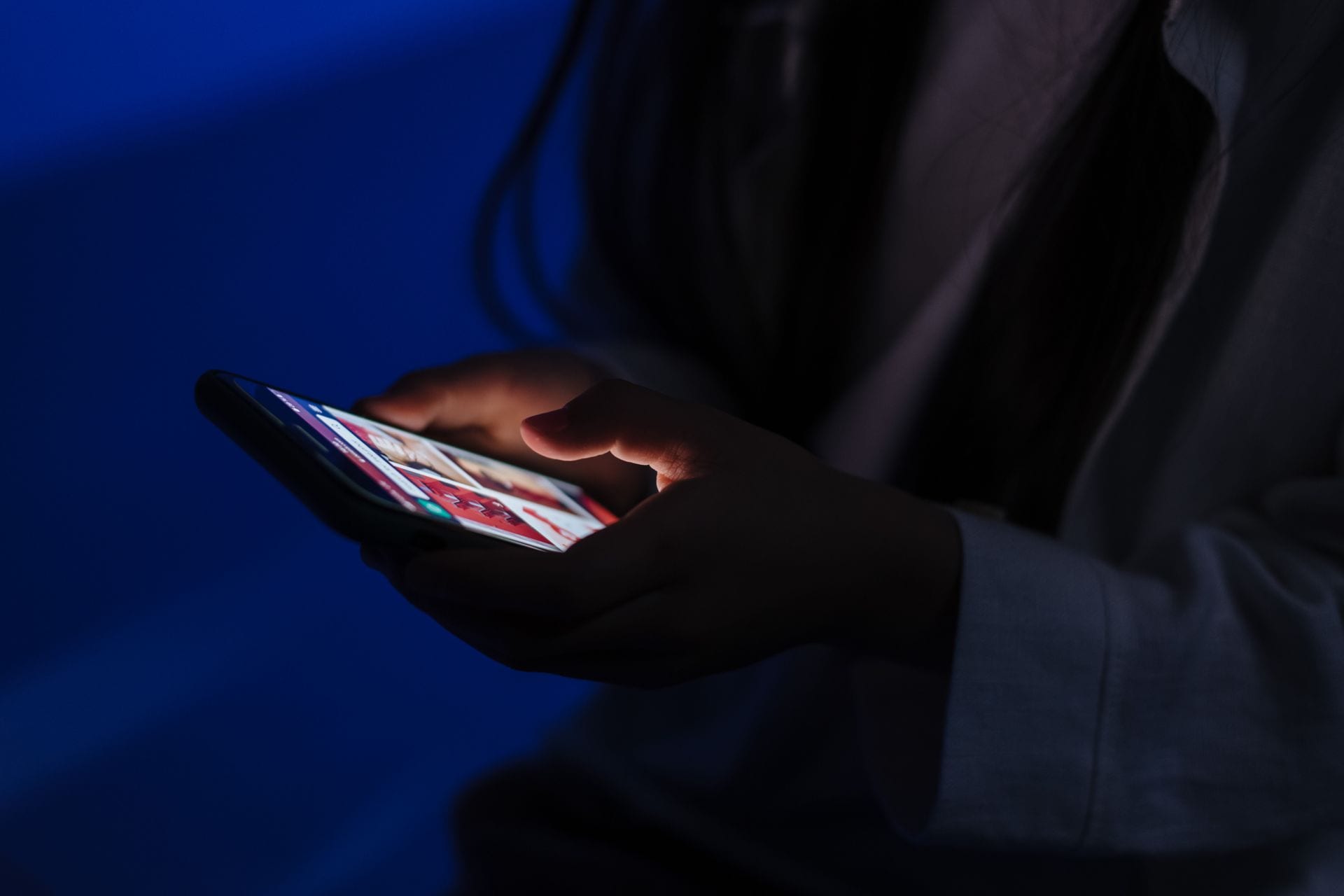 Unas manos sostienen un teléfono con la pantalla encendida en la penumbra, sin rostro visible.