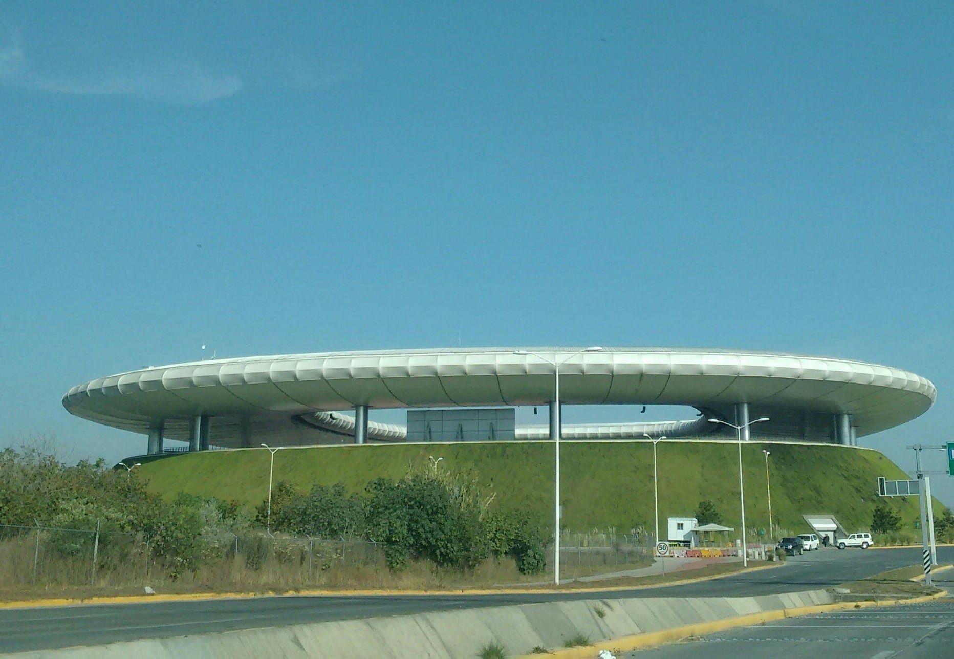 Vista exterior del Estadio Akron, con su techo circular elevado sobre un montículo de pasto, vista desde la carretera.