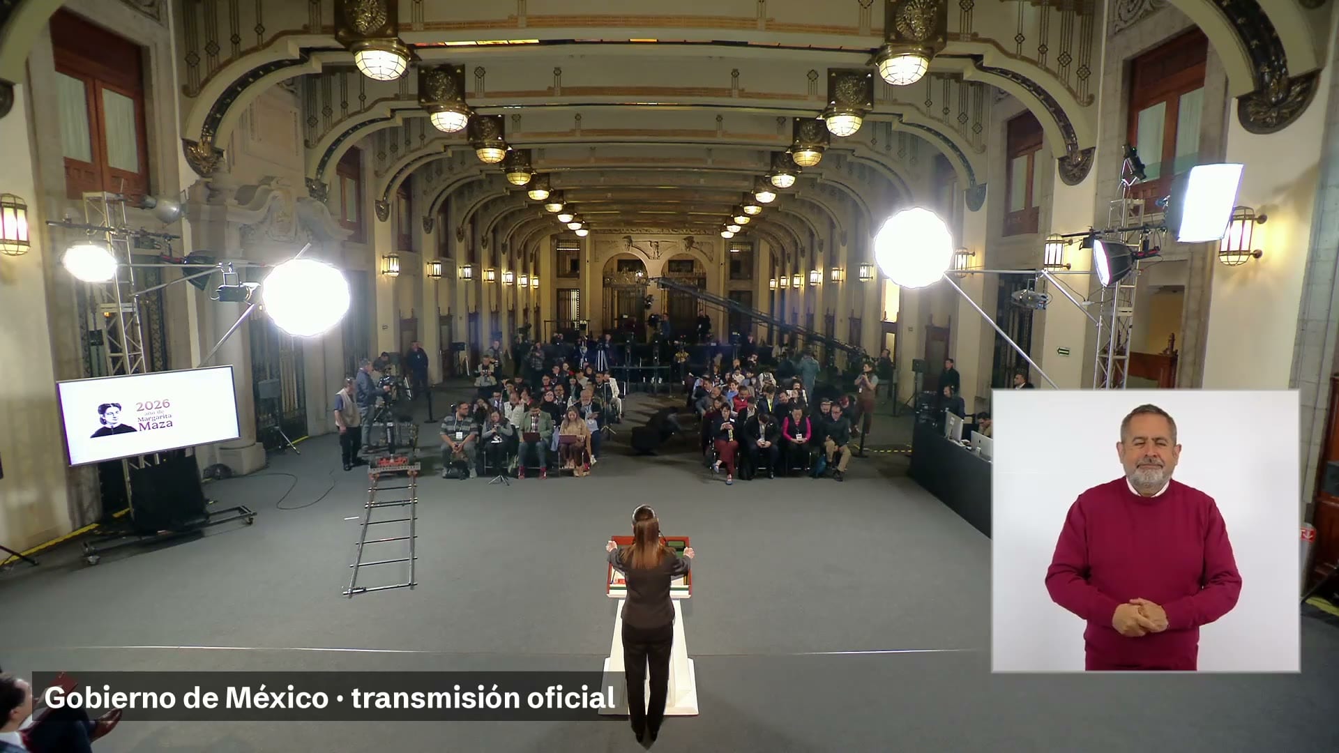 La presidenta Claudia Sheinbaum, de espaldas en el atril, frente a reporteros sentados en el salón de la conferencia matutina.