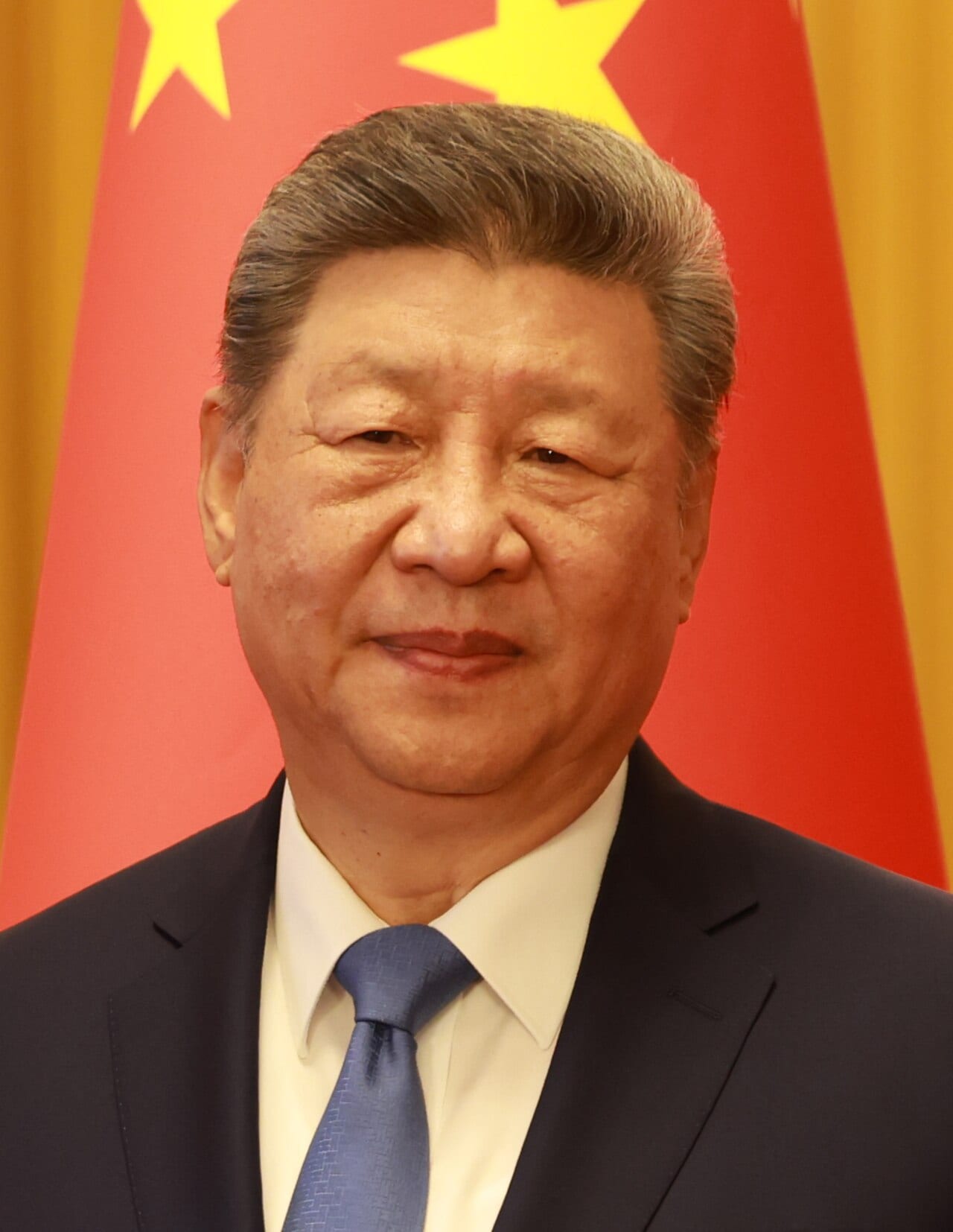 Retrato del presidente chino Xi Jinping, con traje oscuro y corbata azul, frente a la bandera roja de China.