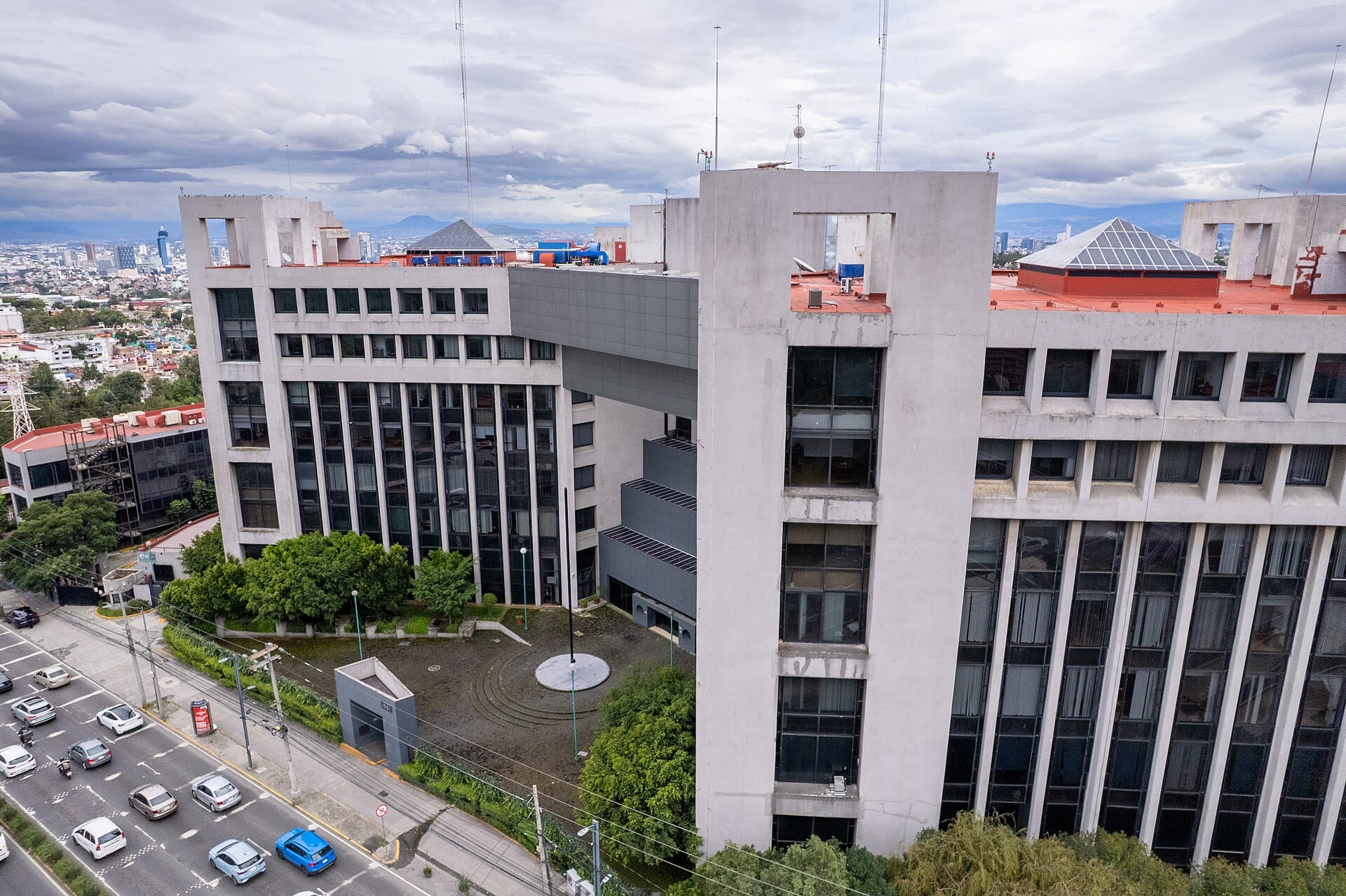 Vista aérea de un edificio de oficinas de concreto y vidrio junto a una avenida con autos.