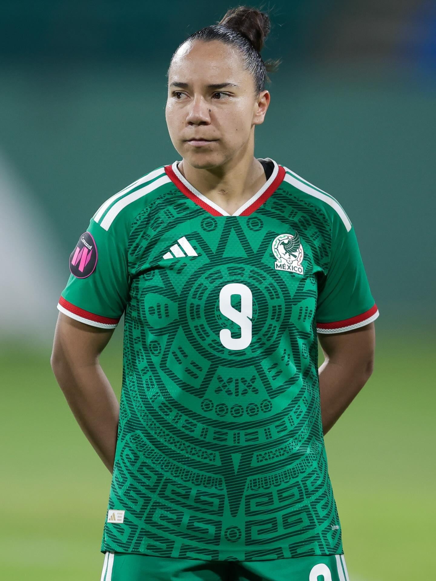 A soccer player with her hair tied back, wearing Mexico's green number 9 jersey, looks off to the side in a stadium.
