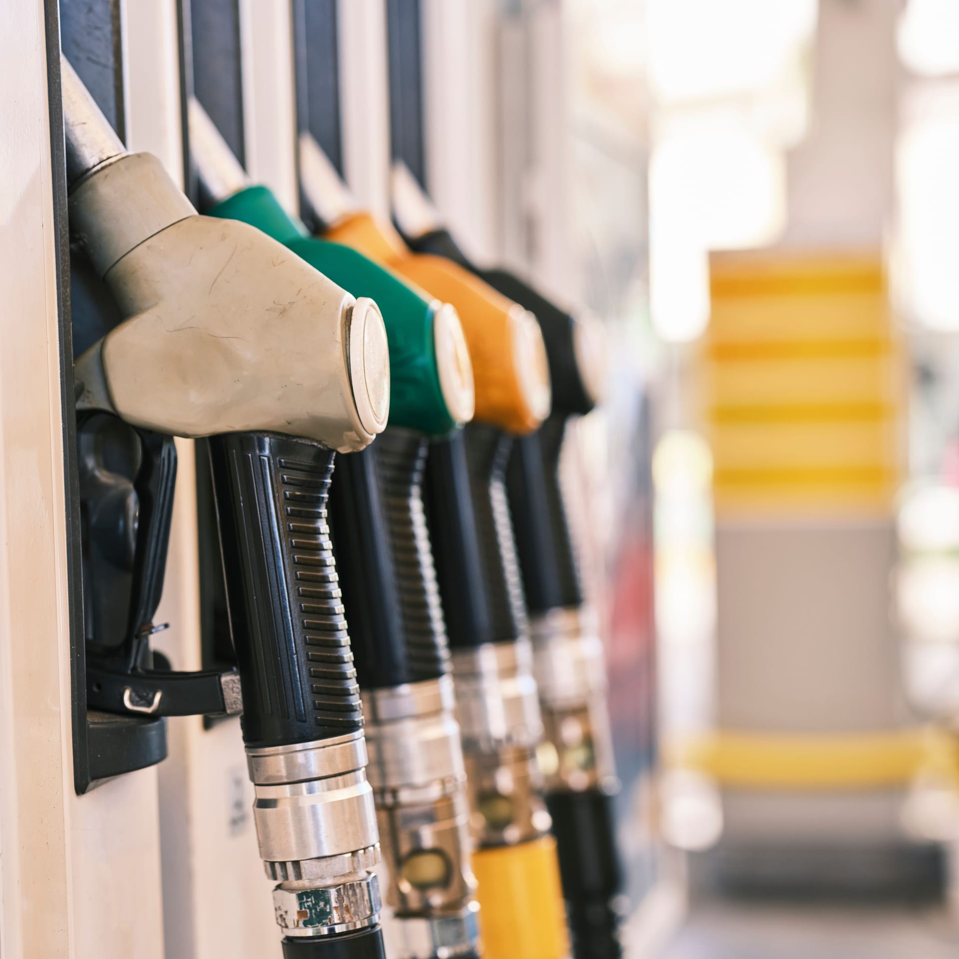 Varias boquillas de despachador de combustible, de distintos colores, alineadas junto a los surtidores de una gasolinera.