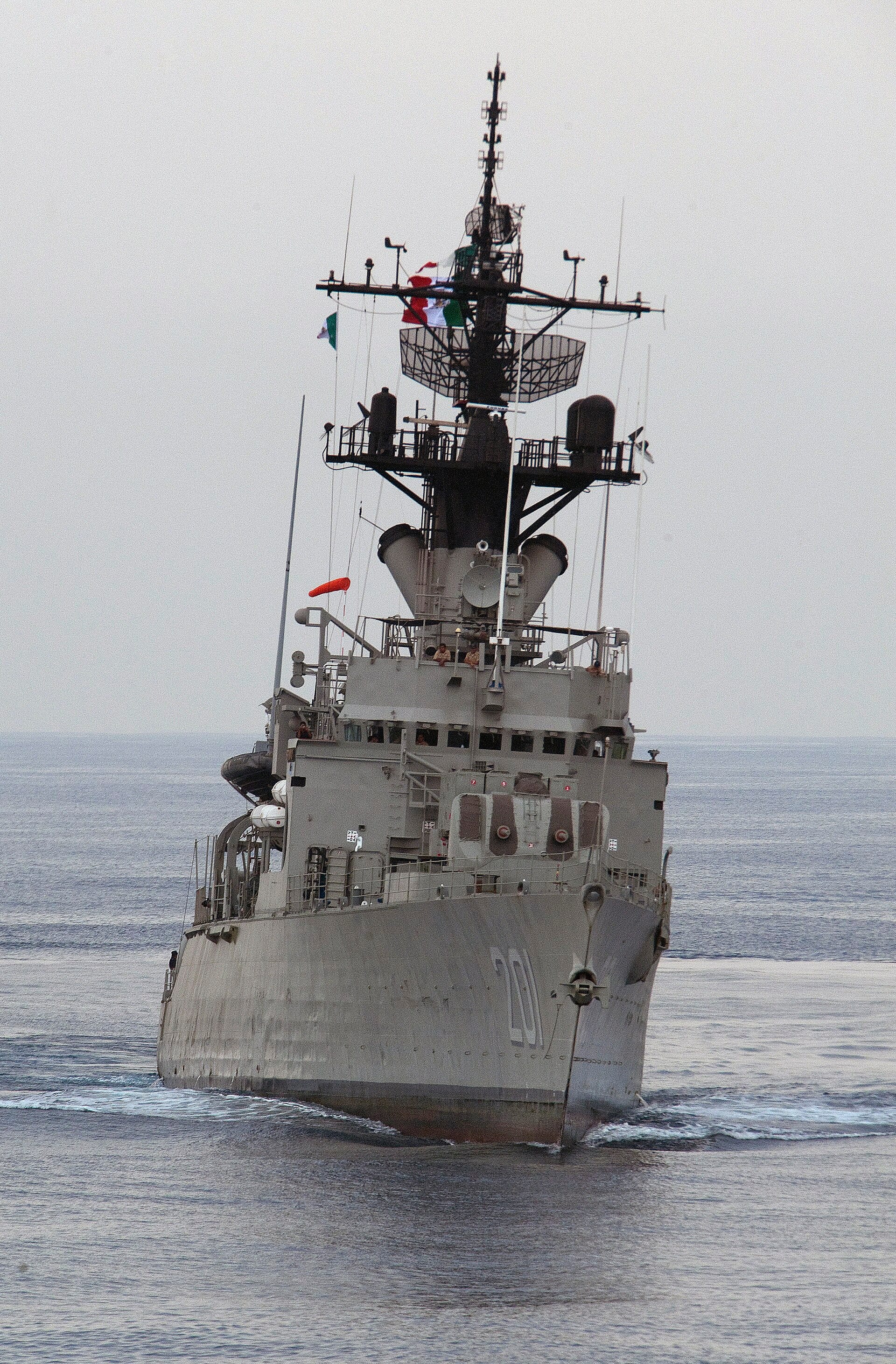 Fragata de la Marina de México, con el número 201 en el casco, navega de frente sobre aguas tranquilas con banderas mexicanas en el mástil.