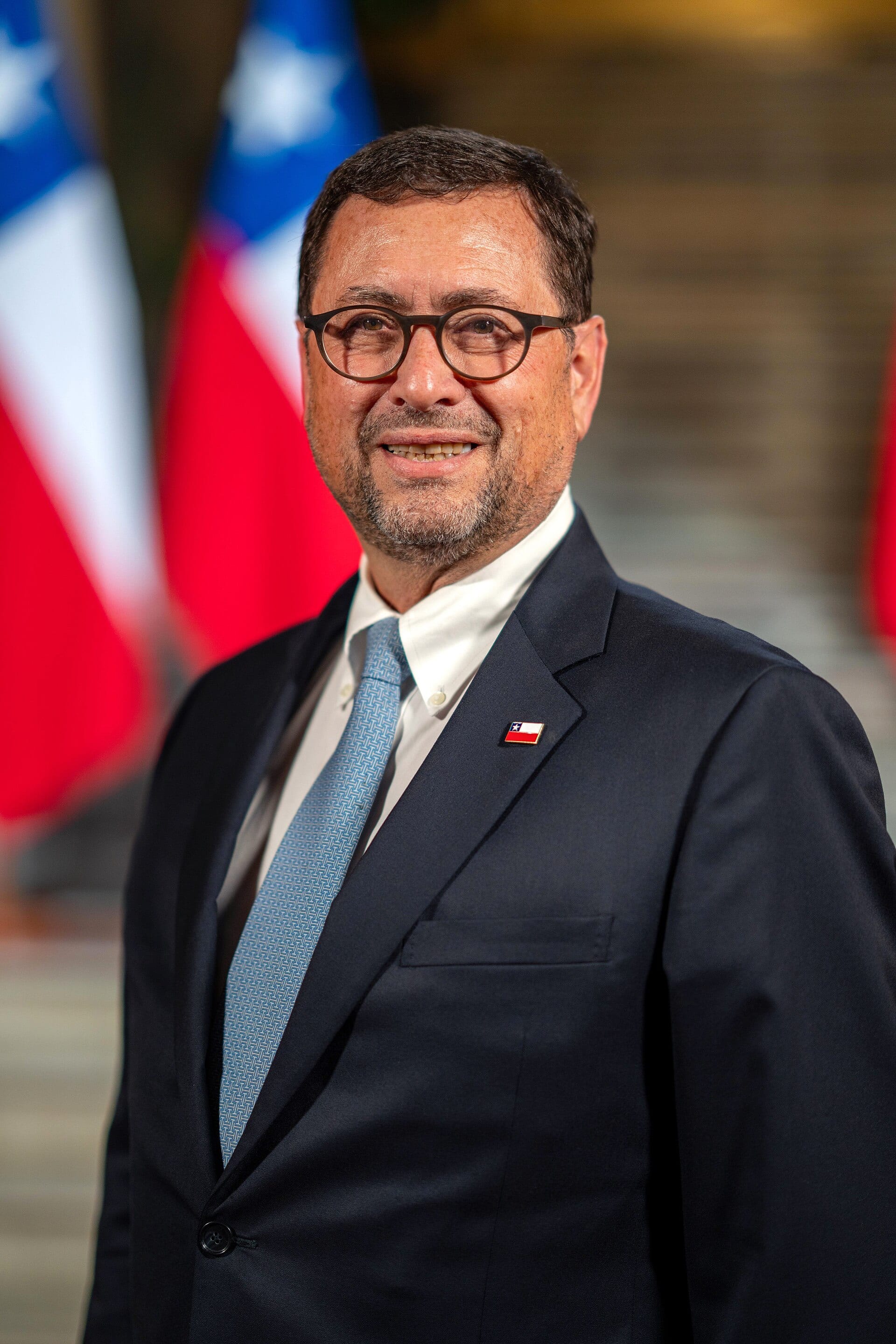 Francisco Pérez Mackenna, de traje oscuro, posa serio frente a banderas de Chile.