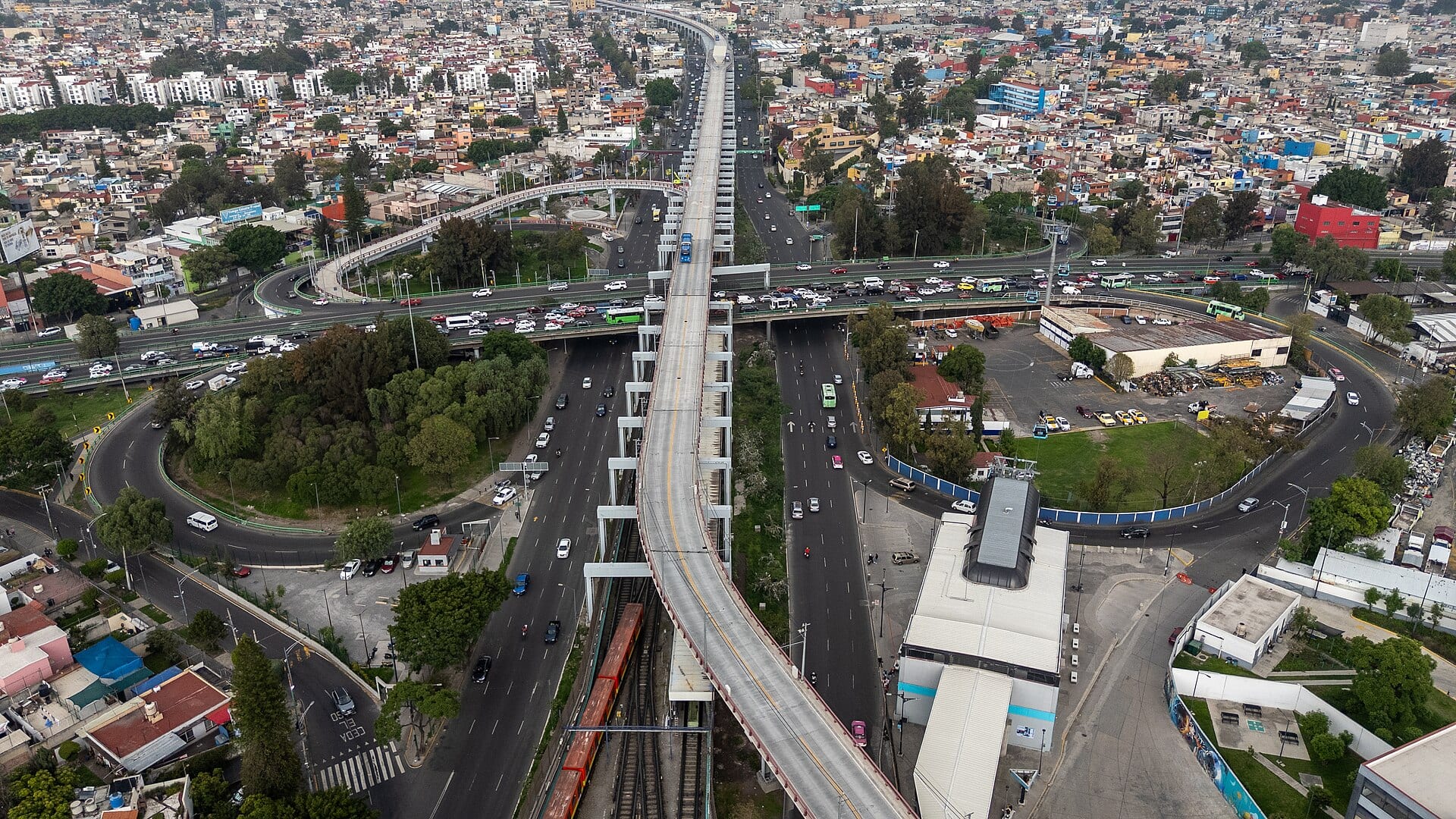 Vista aérea de un cruce de vías rápidas en Iztapalapa, con una fila de autos en el paso elevado y una línea de transporte elevada al centro.