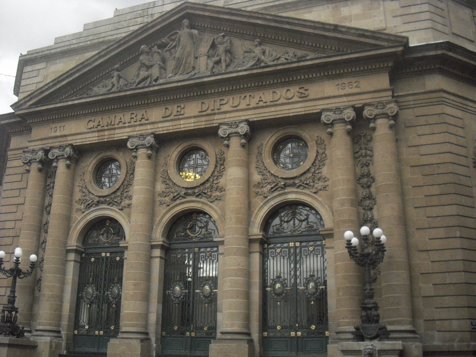 Fachada de piedra con columnas, relieves en el frontón y puertas de herrería, con la inscripción Cámara de Diputados.