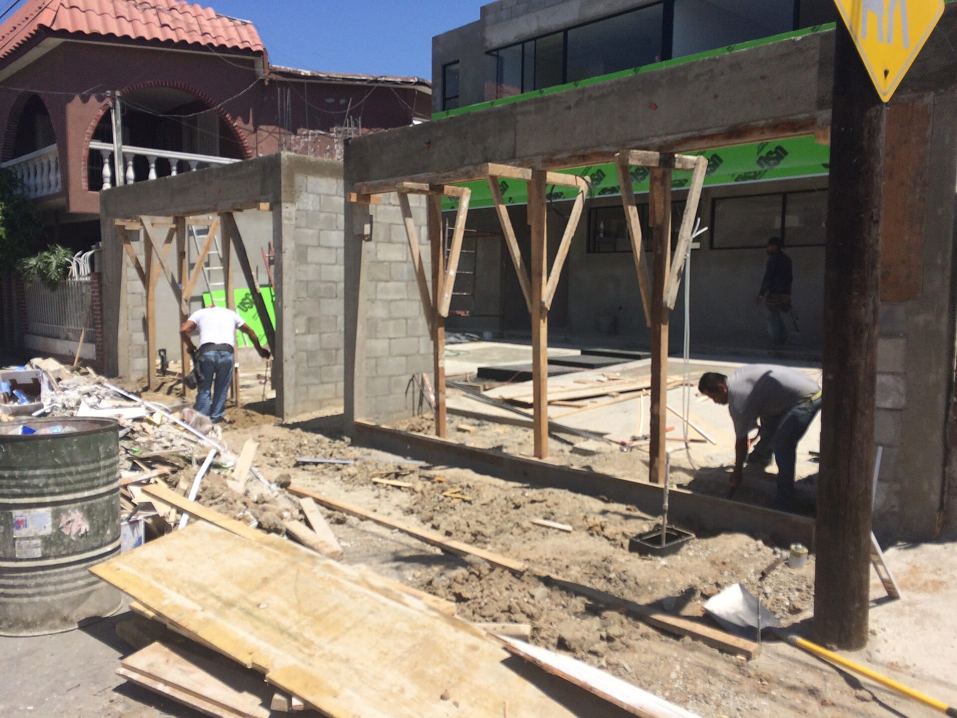 Dos obreros trabajan en la obra de una casa en construcción, con muros de block y cimbra de madera, en una calle de Tijuana.