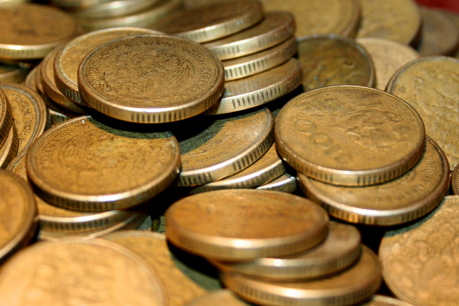 Un montón de monedas doradas de pesos mexicanos, apiladas y fotografiadas de cerca.