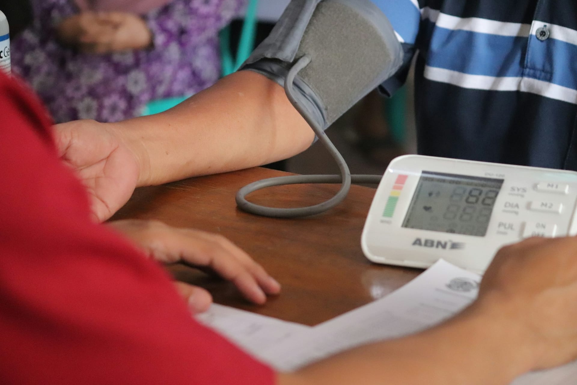 Un tensiómetro digital de brazo sobre una mesa, con el brazalete enrollado junto a la pantalla del aparato.