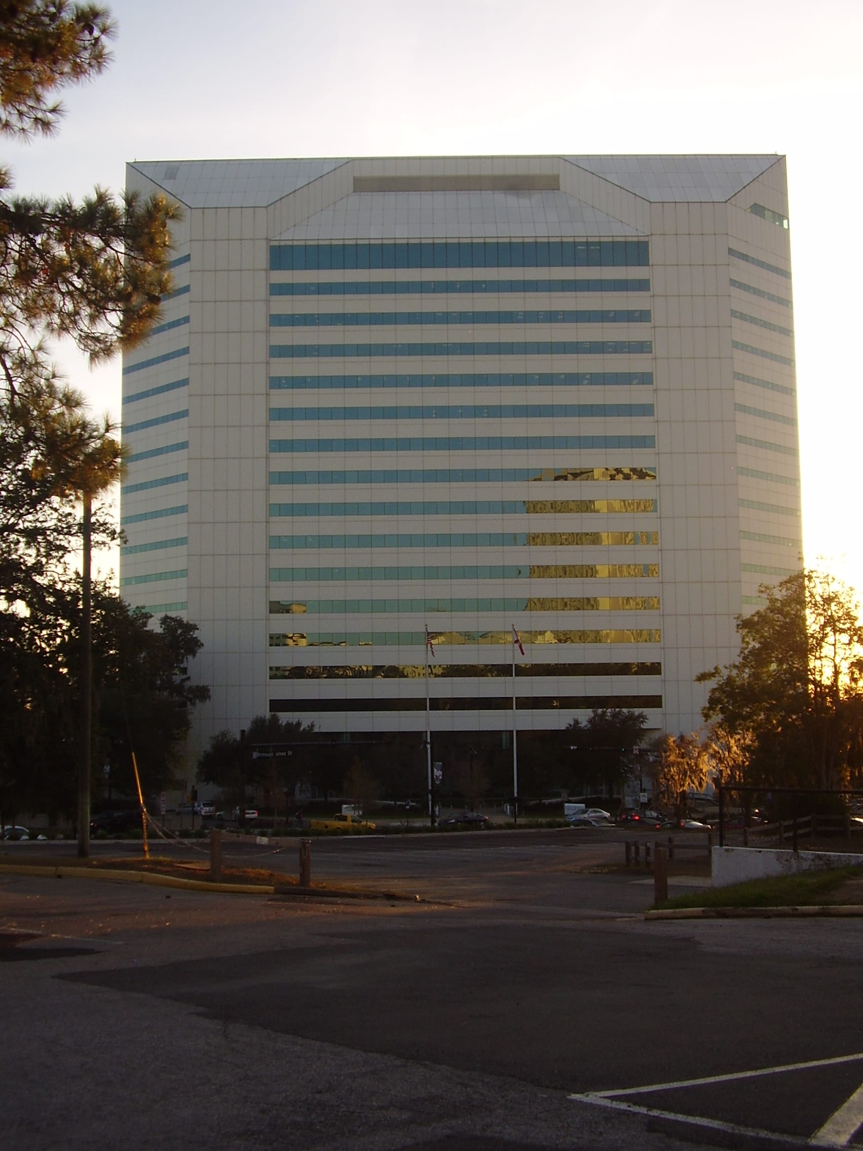 Fachada del edificio Turlington, de más de una docena de pisos con franjas de ventanas azules, con dos astas de bandera al pie y árboles a los lados.