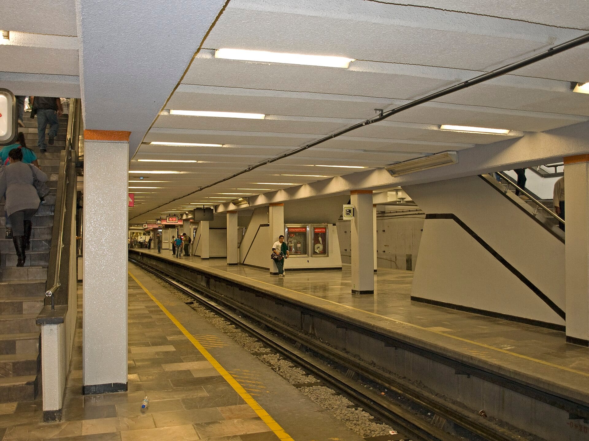 Un andén subterráneo de la estación Pantitlán del Metro, con pasajeros caminando junto a las vías y una escalera al fondo.
