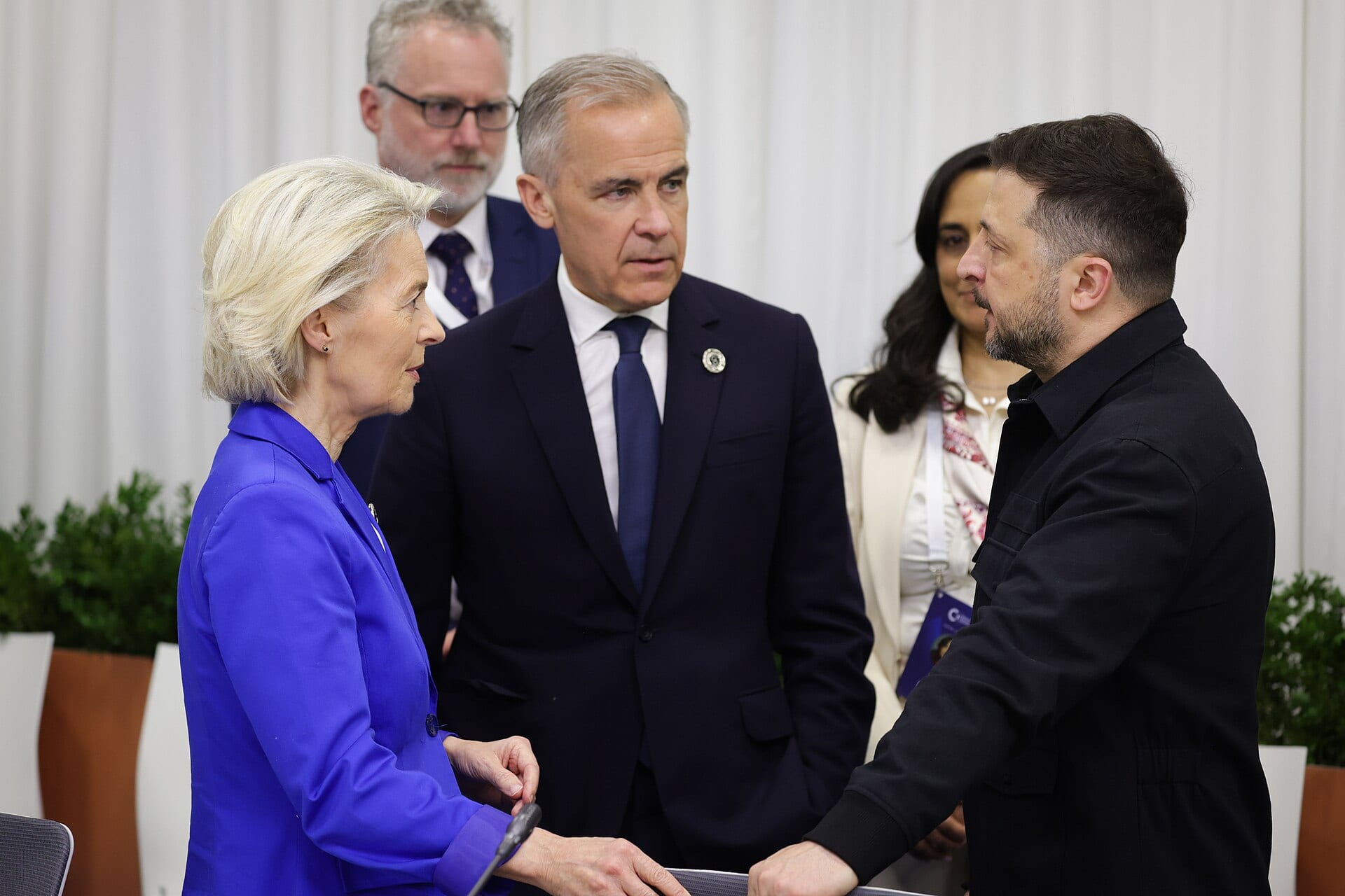 Volodymyr Zelensky, in a dark shirt, talks standing up with Ursula von der Leyen, in a blue jacket, and Mark Carney, in a suit, at a European summit.