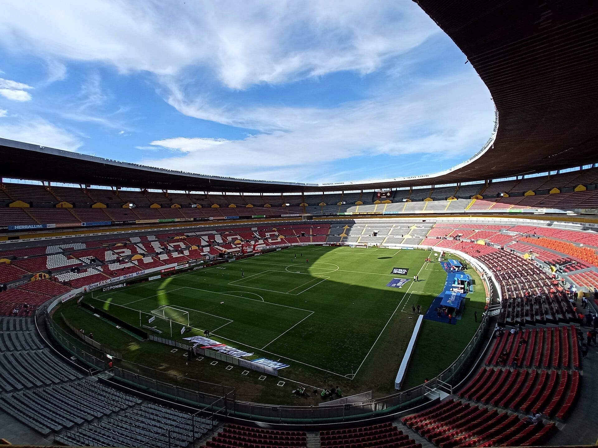 Vista de las gradas del Estadio Jalisco desde lo alto, con el campo de pasto verde y una franja de sombra sobre la cancha.