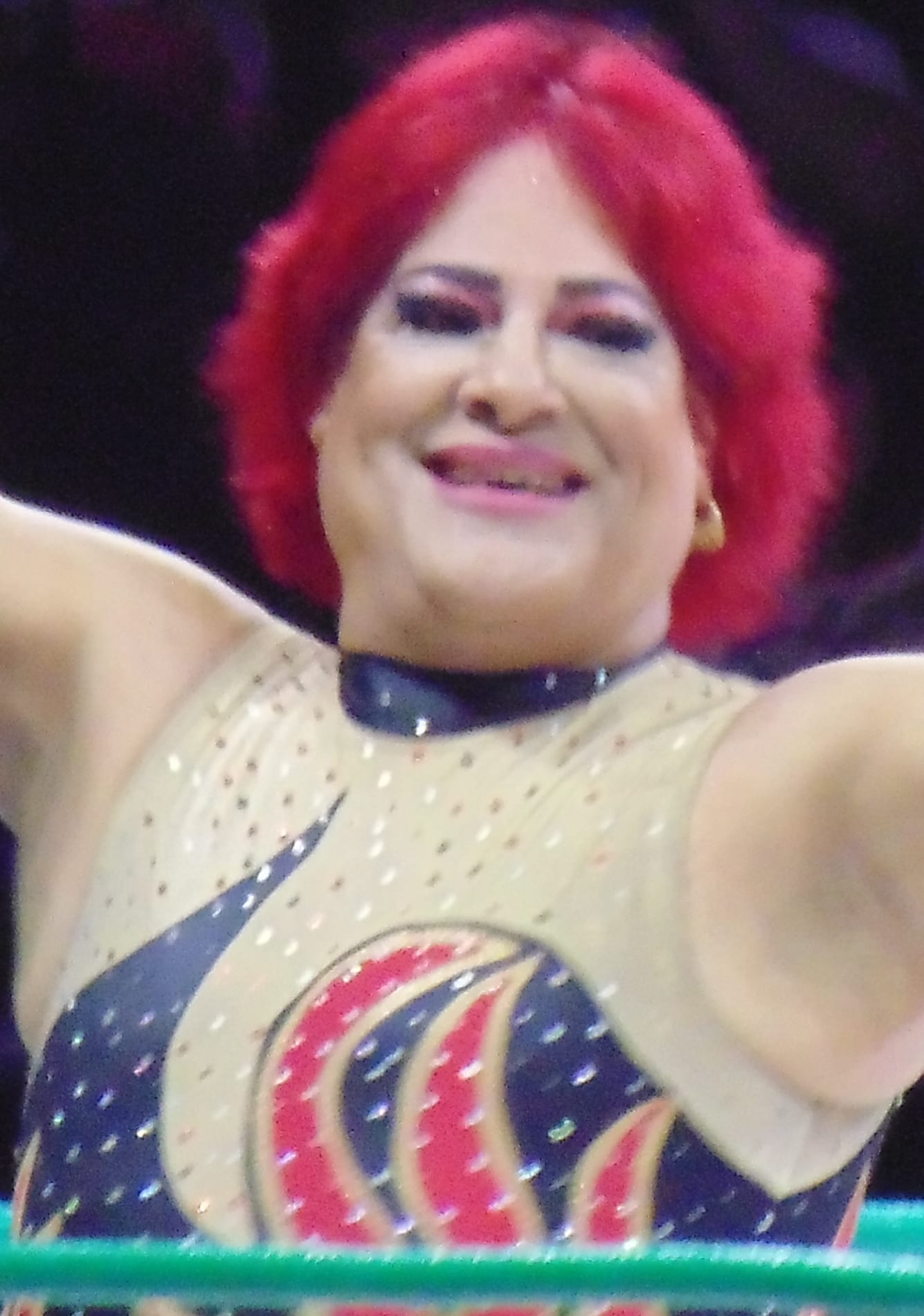 Pimpinela Escarlata, de cabello rojo, sonríe con los brazos en alto en un ring de lucha libre.