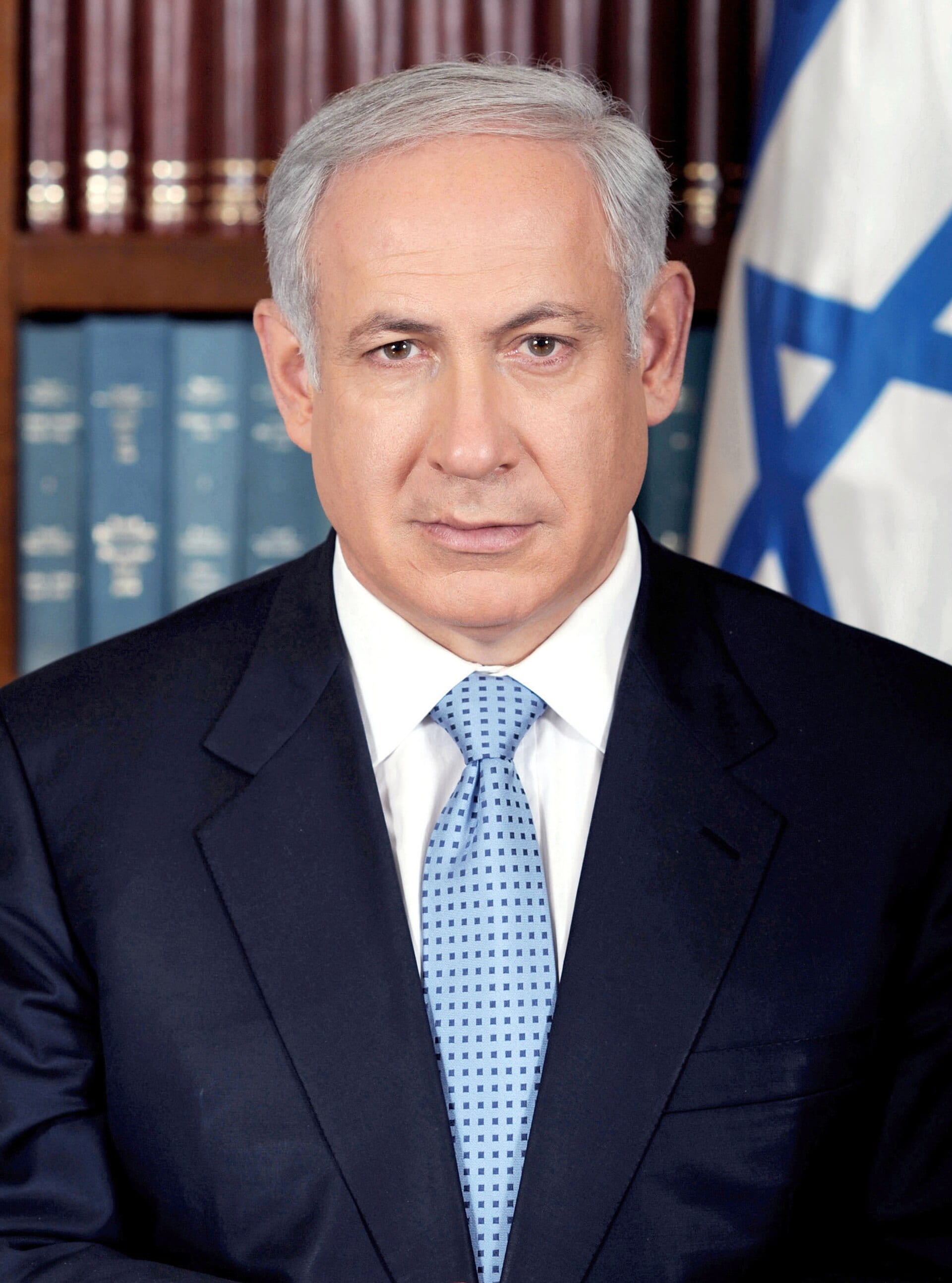 Benjamin Netanyahu, de traje oscuro, mira de frente con la bandera de Israel al fondo.